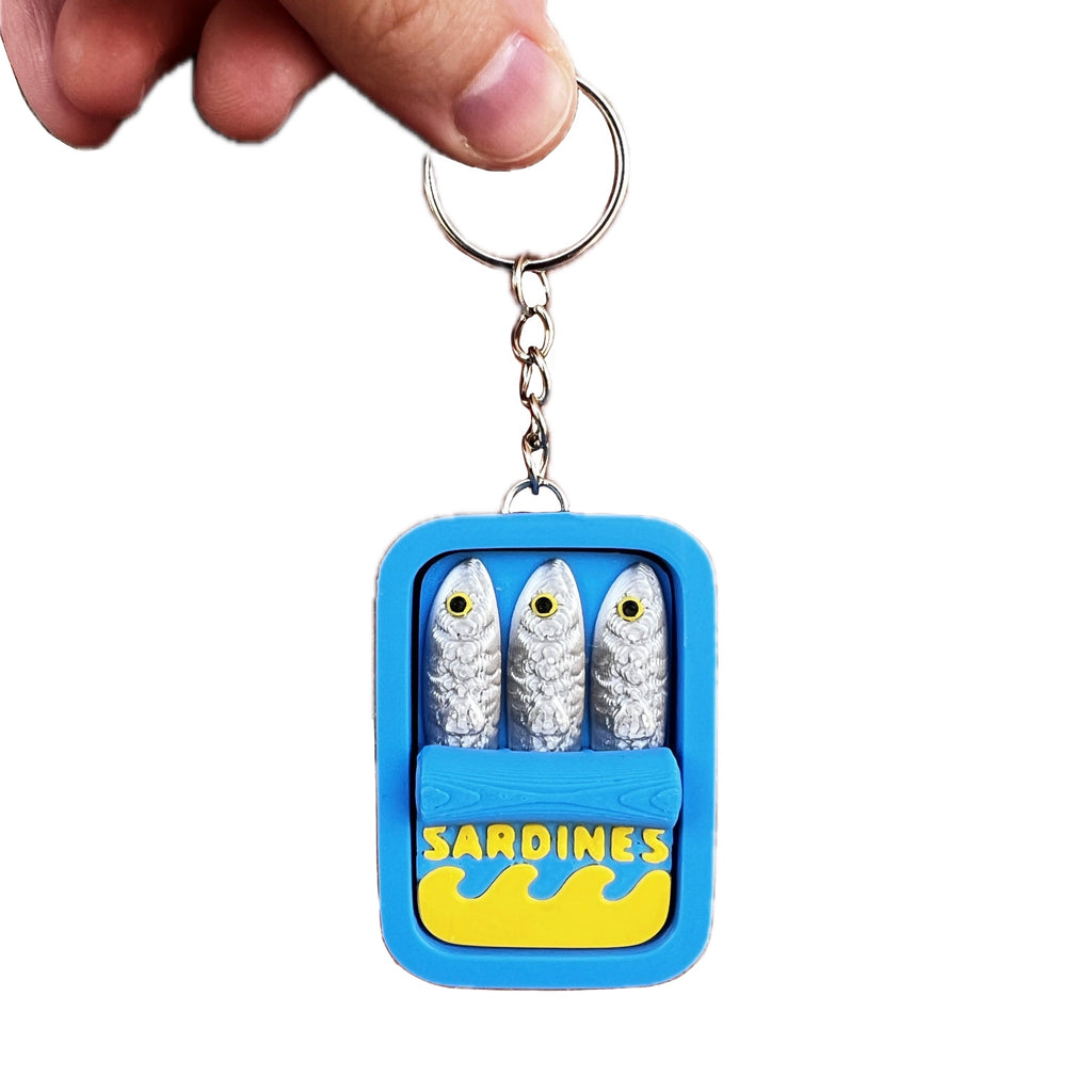 Keychain in the shape of a container labeled 'Sardines' with three small figures on a white background.