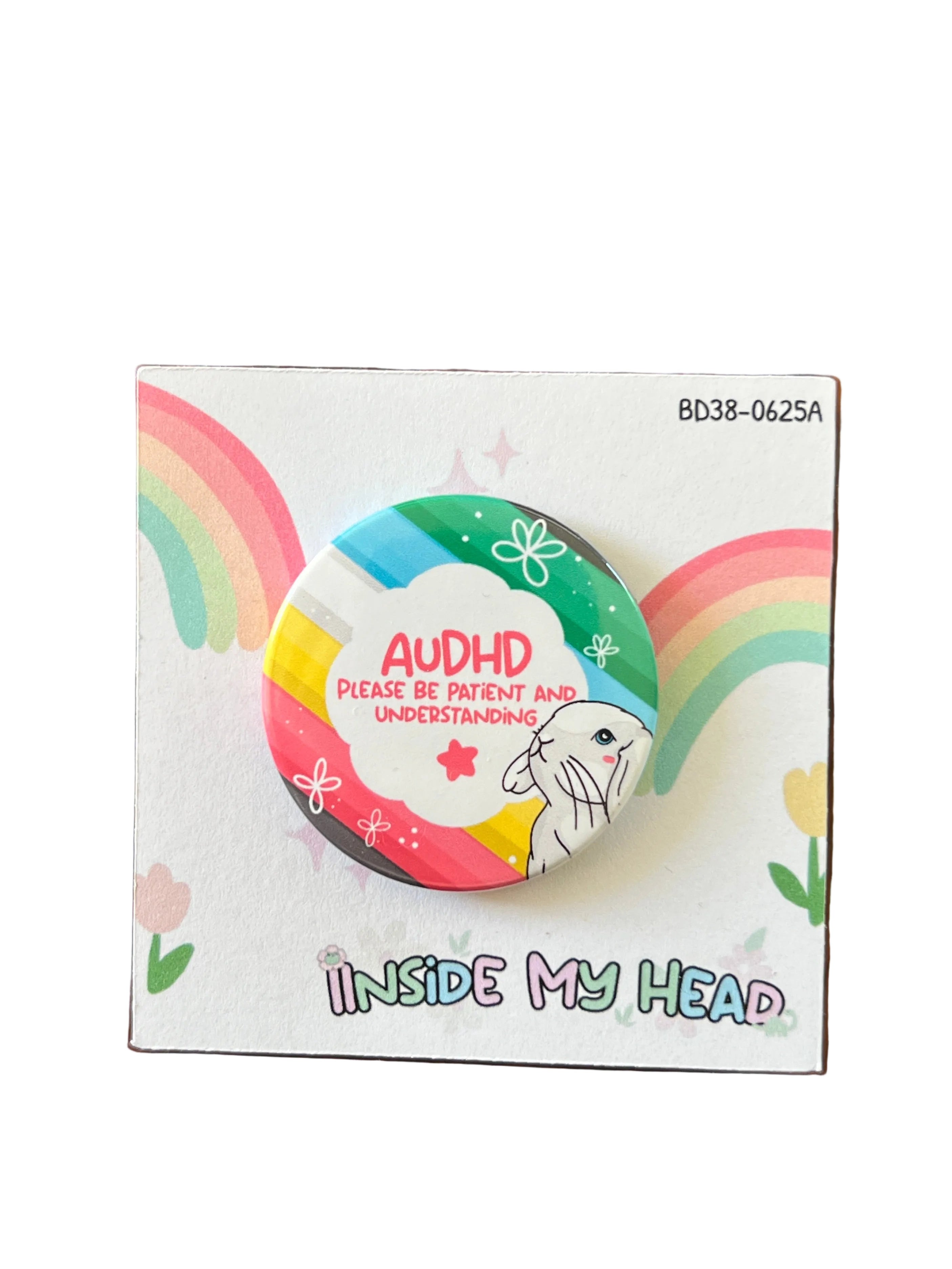 A round pin badge featuring a colorful rainbow design, a white rabbit, and the text 'AUDHD PLEASE BE PATIENT AND UNDERSTANDING', displayed on its printed backing card which reads 'INSIDE MY HEAD' and is photographed on a wooden tabletop.